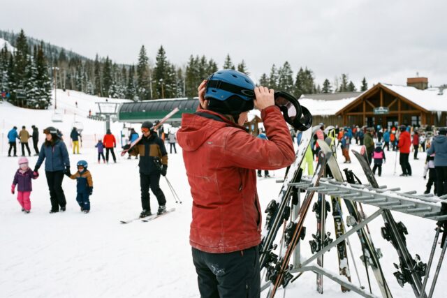 Un skieur ajuste son casque près d'une zone débutants tandis que d'autres personnes circulent en station